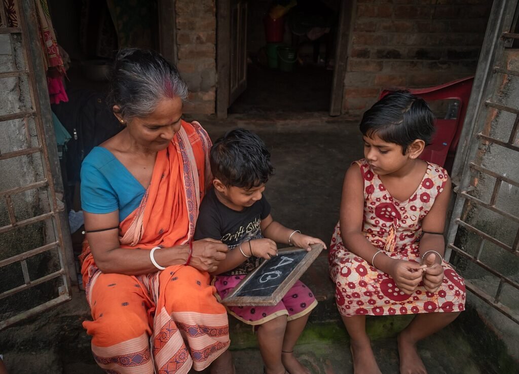 Grandmother helping children practise letters on a slate, learning basic Telugu words for kids